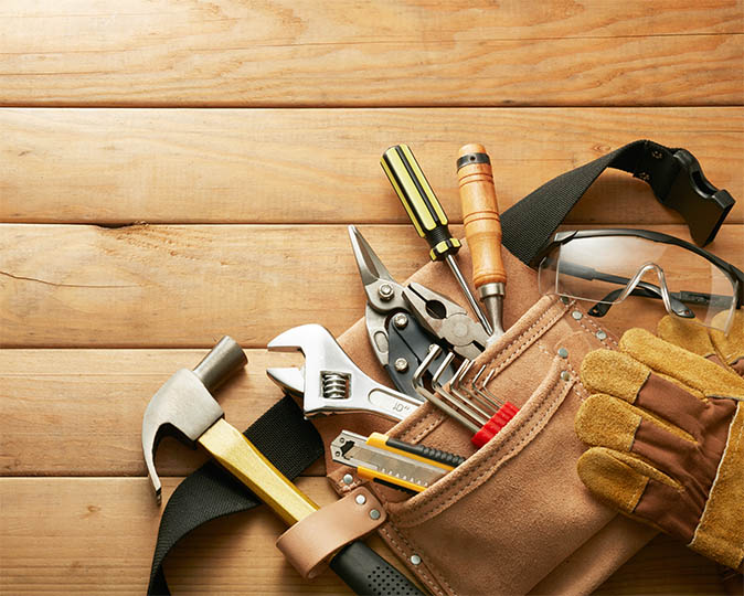A tool belt equipped with home tools, sitting on top of wood panels.