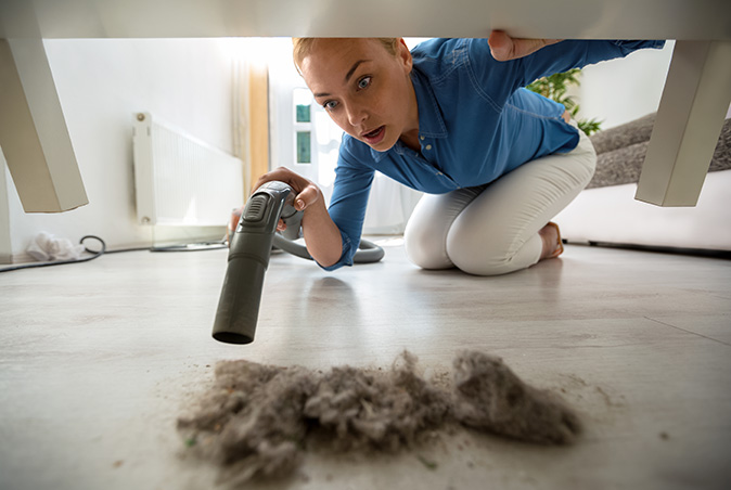 A woman vacuums up dust and dust mites under her furniture.