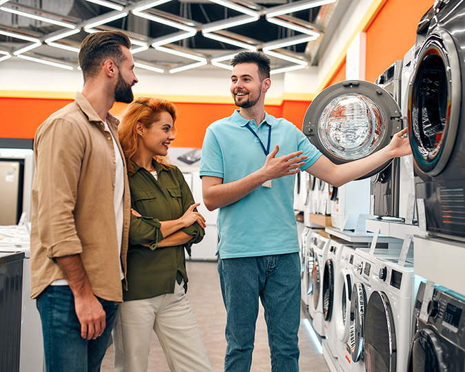 A salesperson discusses the features of a new front-loading washer with a young couple.