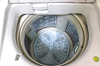 View of washing machine looking into basin with lid button on the left front of the opening