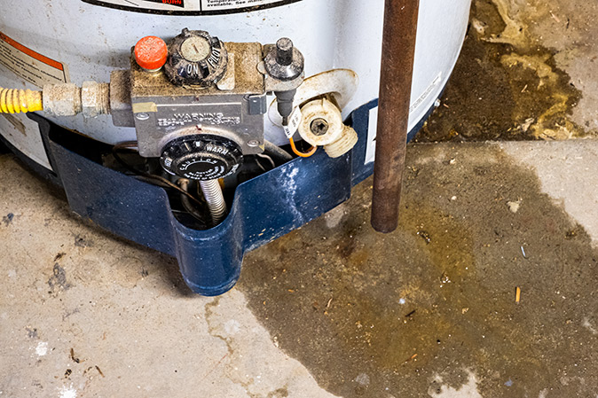 A close-up of a water heater leaking water on a concrete floor.