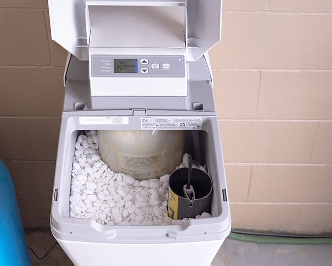 A household water softener with its tank open and a view of the salt pellets.