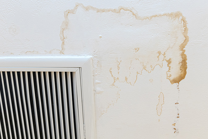 A brown water stain on a white ceiling from condensation on an air vent.