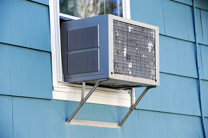 An exterior view of a window air conditioning unit outside of a blue house.