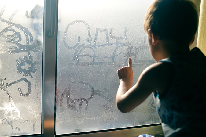 Closeup of a child drawing on the condensation on a window at home.
