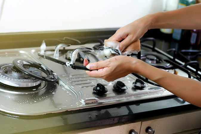 A woman deep-cleans her gas stove, including the grates.