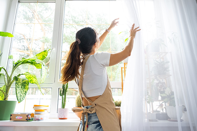 A homeowner installs wispy white curtains to fill her living room with natural light.