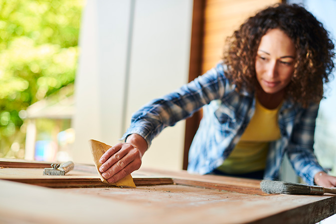 A woman sanding a wooden door to fix the dent.  