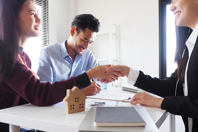 A couple signs the contract on their new home and shakes hands with their real estate agent.