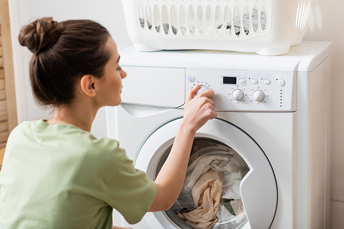 A woman starting a load in her washing machine.