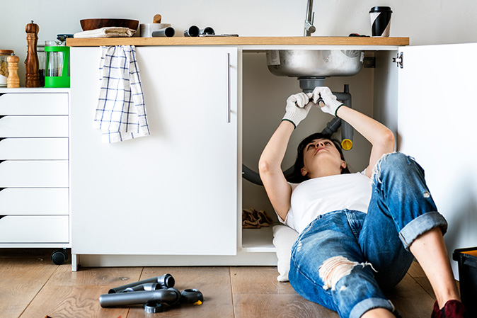 Woman lying on the floor fixing the kitchen sink. 