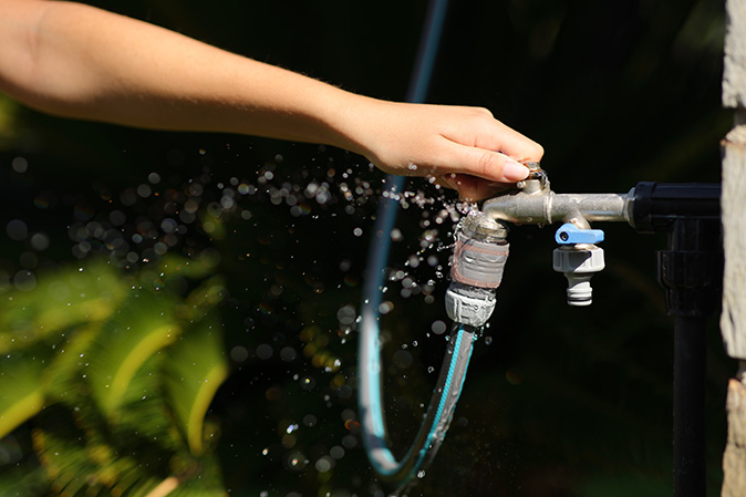 A woman’s hand opening an outdoor faucet with a water leak.