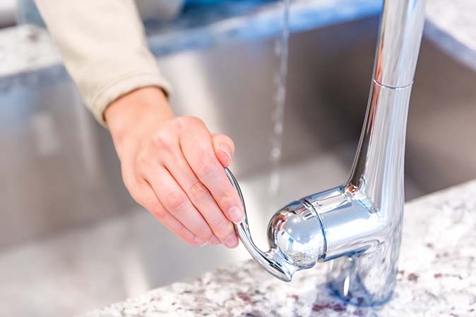 A woman’s hand turning on a faucet in a brightly lit kitchen.