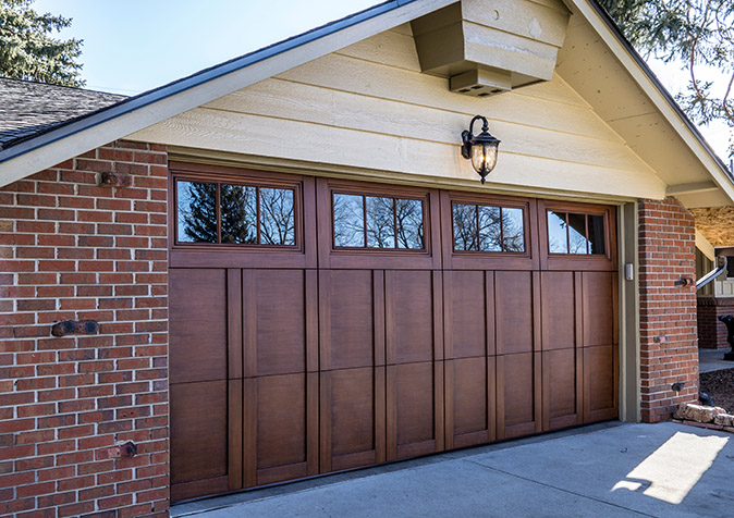 A custom wood garage door attached to a brick- and shiplap-sided house.